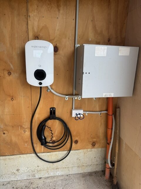 Wall-mounted Sigenergy EV AC charger on plywood backing