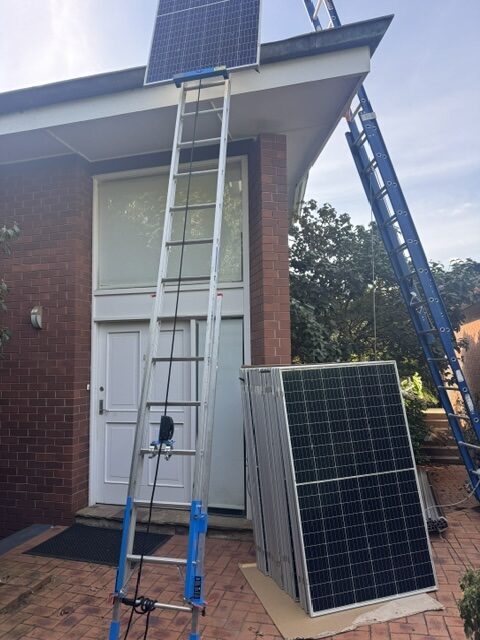 A solar panel being lifted to a roof on a ladder hoist